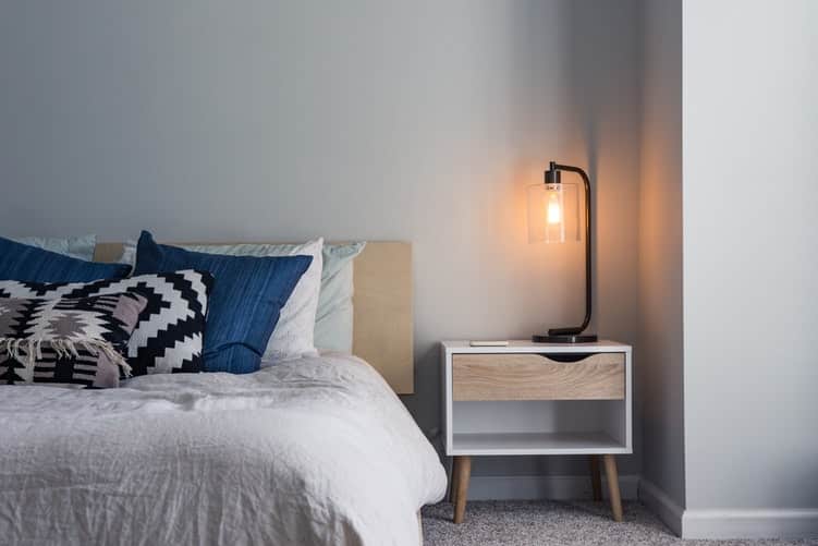 image of bed, pillows, nightstand and lamp. money saving tips for first-time renters