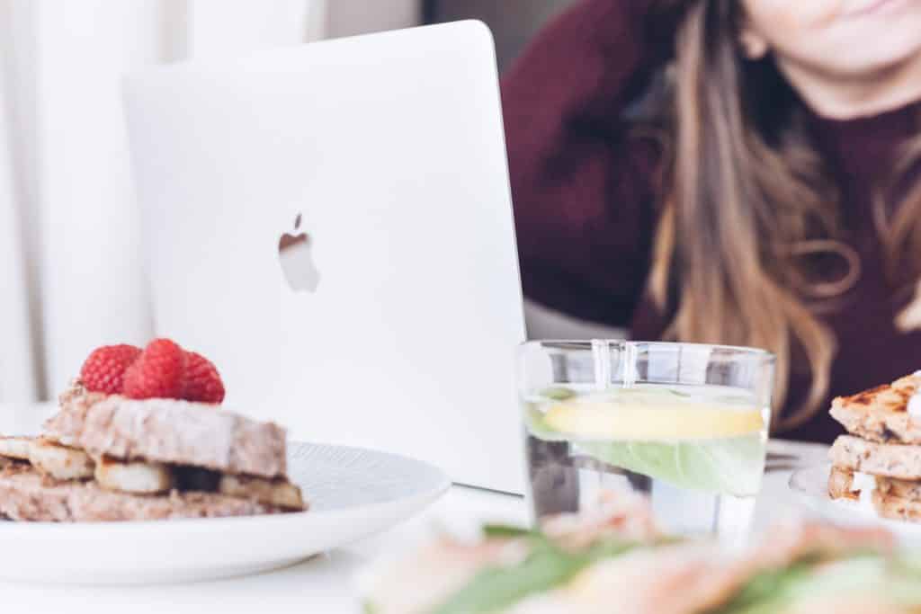 save money for christmas by bringing your lunch to work. Image of woman working on laptop with lunch in background