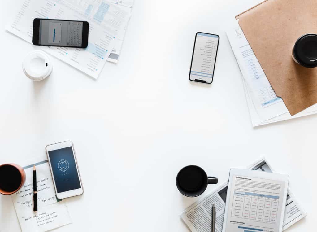 cell phones and notepads with budget sheets on a table with coffee