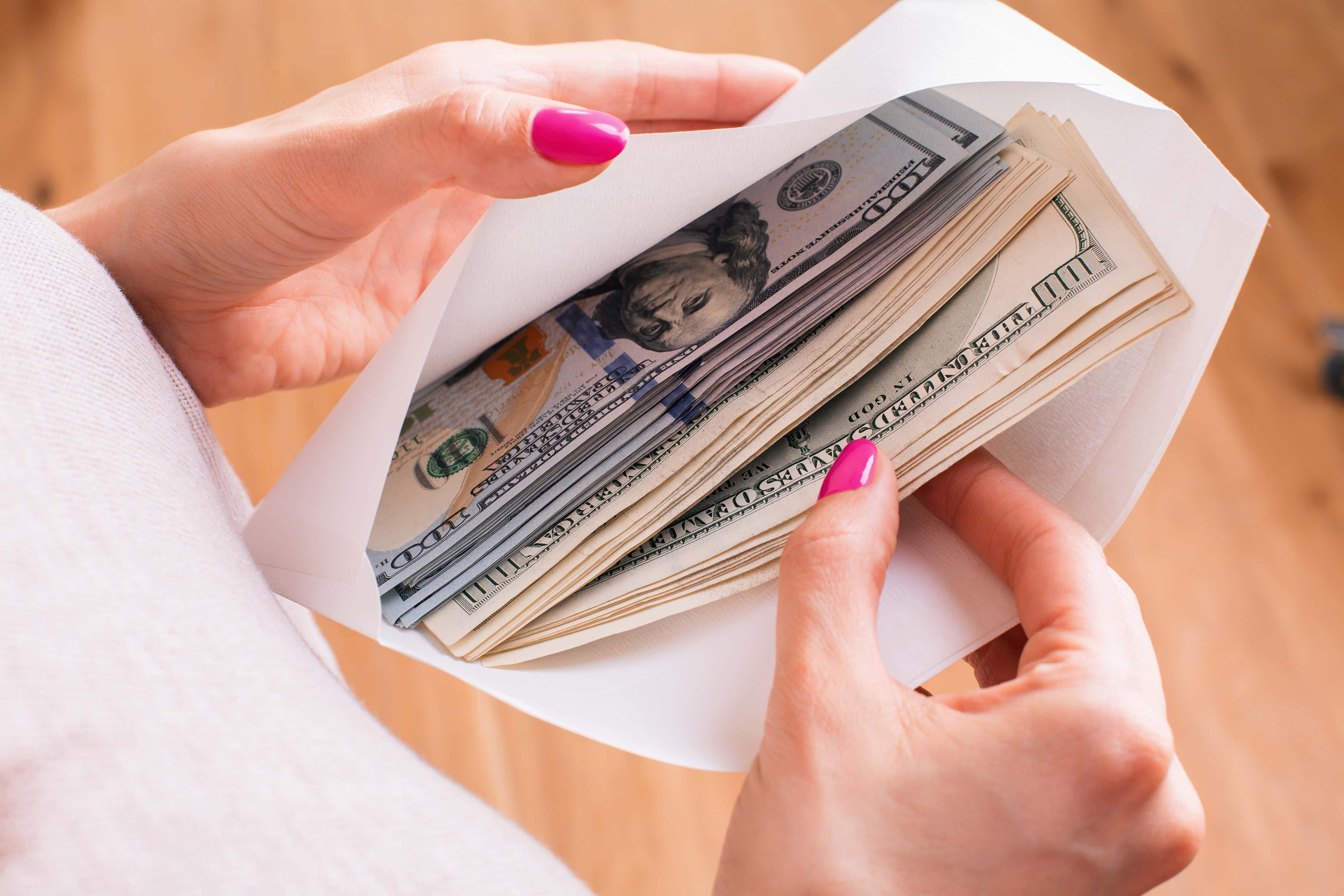 Frugal living tips for cash envelopes. Photo of woman with pink painted nails taking out money from an envelope.