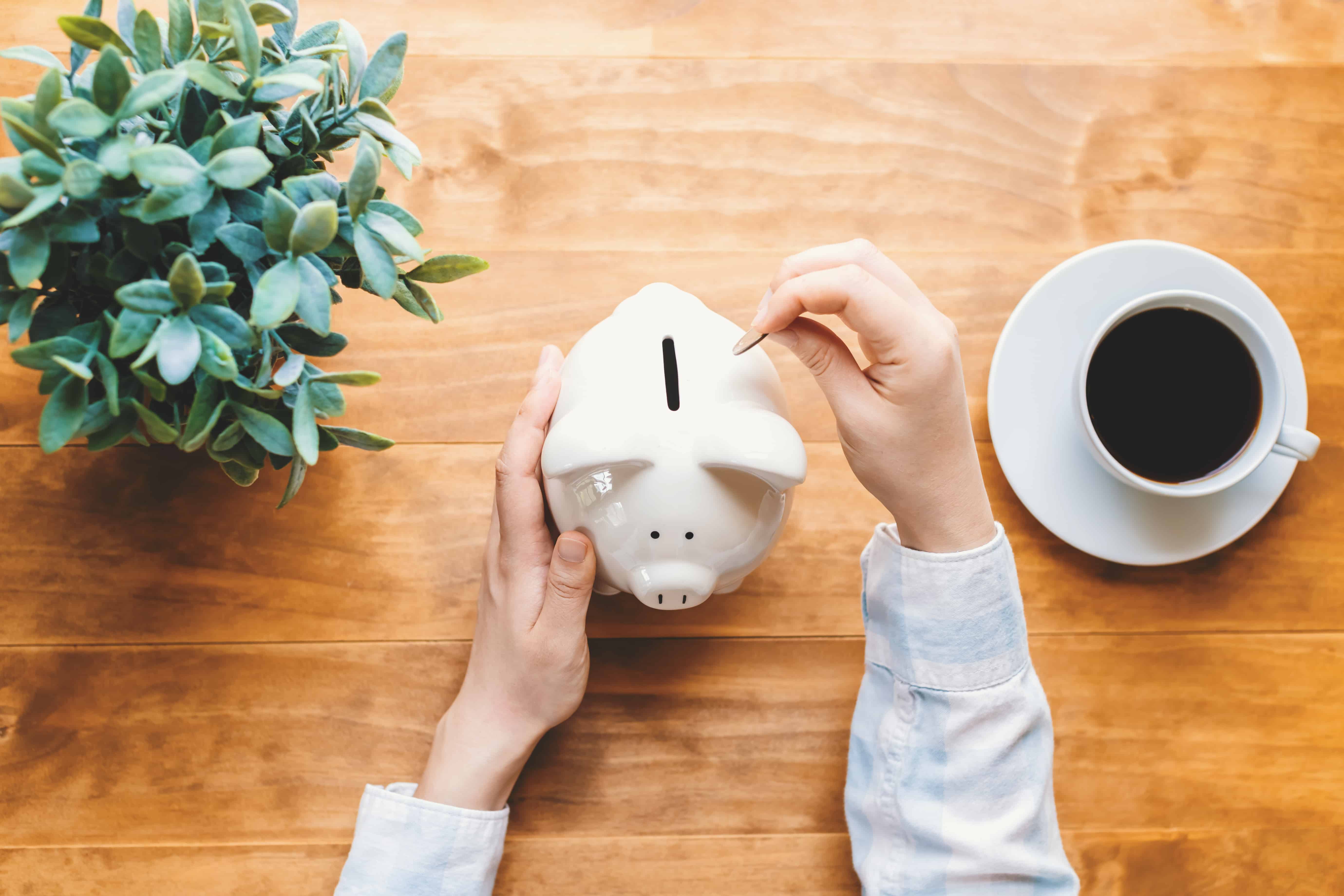 frugal living tips for saving money. Photo of person putting a coin into a white piggy bank.