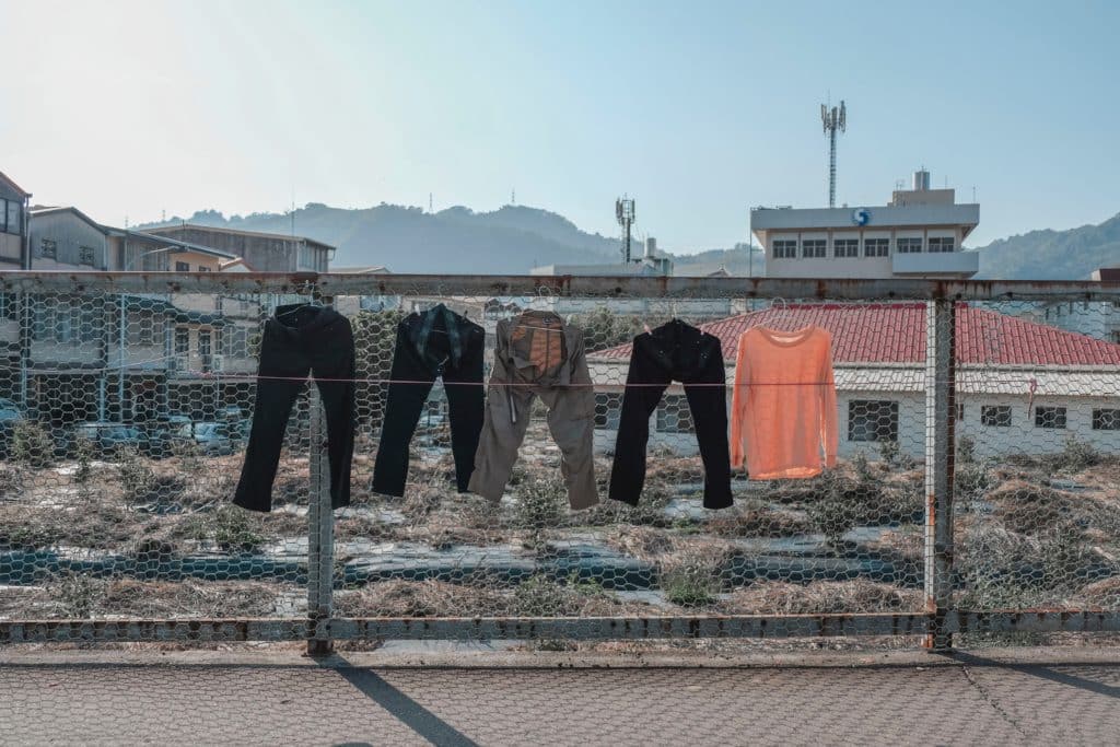 Things we waste money on clothing pic. Pants and tops hanging on a wire fence.