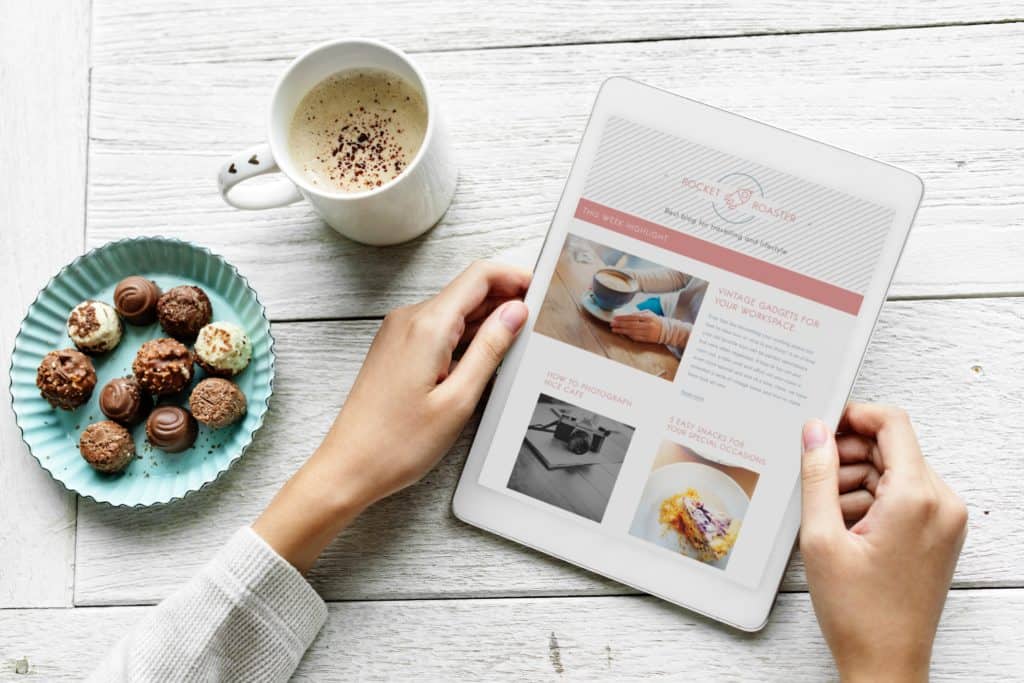 Pay off debt ideas - start a blog. image of woman on tablet with cup of coffee they and chocolate biscuits.
