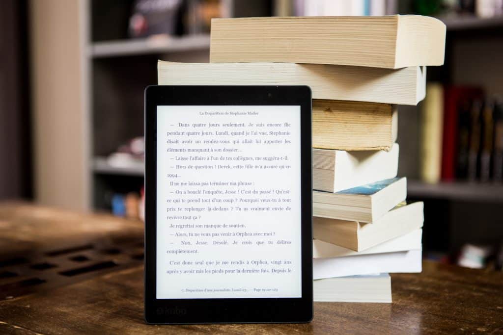 A tablet and books on a desk with bookshelf in background.