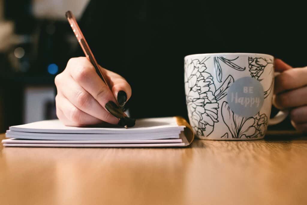 best work from home jobs writer image of woman journaling with pen and cup of tea in hand.