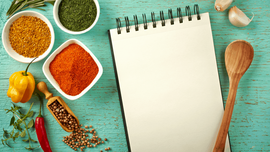 Spices, vegetables, notebook, and wooden spoon on a table